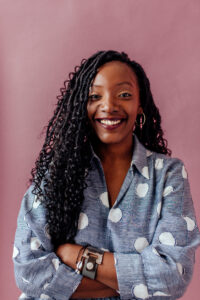 Image Description: Nassy is a Black woman with long black hair with loose curls, a big smile and burgundy lippy on.